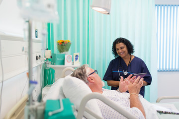 Smiling doctor making rounds, talking with senior patient in hospital room