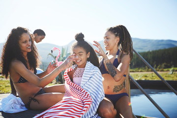 Playful lesbian couple putting sunscreen on daughter at sunny, summer poolside