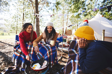 Lesbian couple and kids cooking breakfast at campsite grill in woods