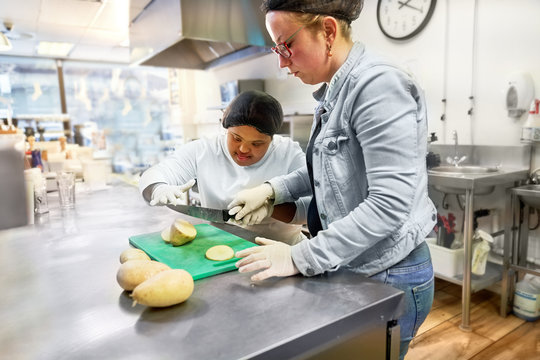 Chef and young woman with Down Syndrome cutting potatoes in cafe