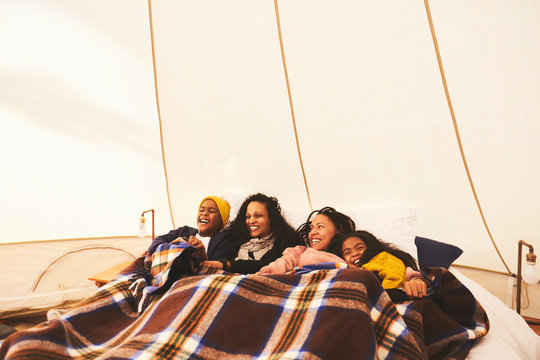 Happy lesbian couple and kids relaxing under blanket in bed in camping yurt