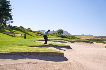Male golfer taking a shot above sunny sand trap