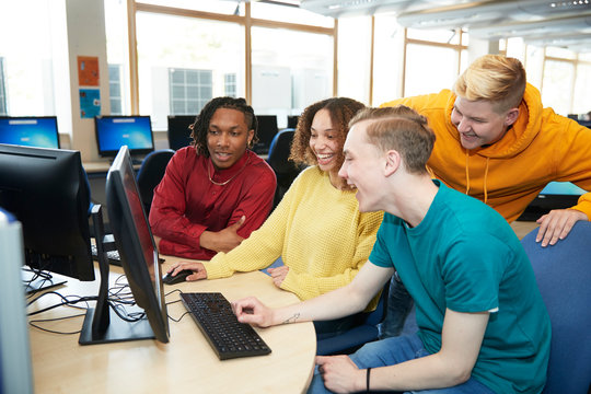 Happy young college students using computer together in library