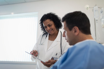 Doctor with digital tablet making rounds, talking with patient in hospital room
