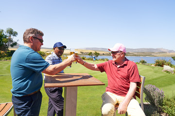 Mature male golfers drinking beer on sunny golf clubhouse patio