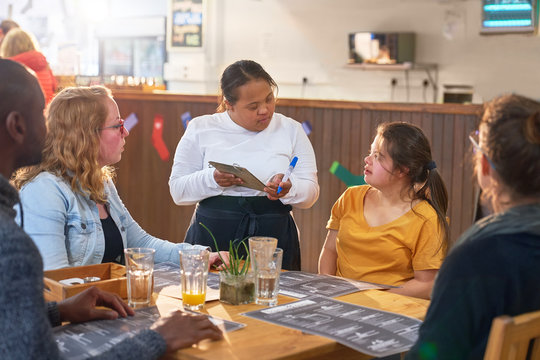 Young female server with Down Syndrome taking order in cafe