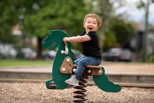 Carefree cute toddler girl riding dinosaur toy at playground