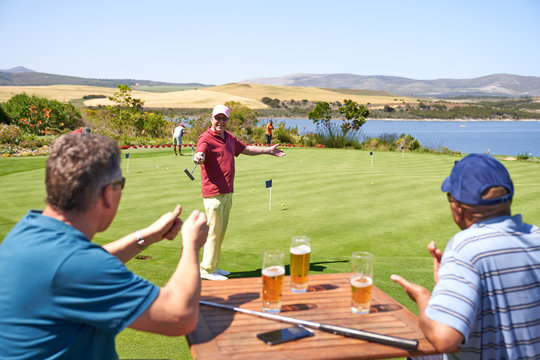 Happy male golfers drinking beer and practicing putting at golf course