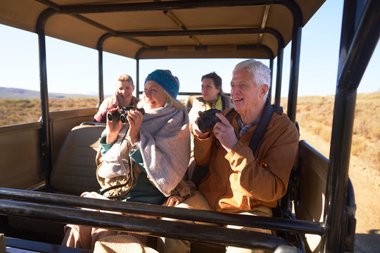 Happy seniors with binoculars and camera on safari in off-road vehicle