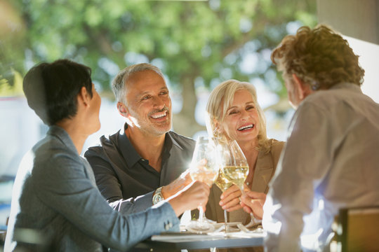 Couples toasting white wine glasses at sunny restaurant table