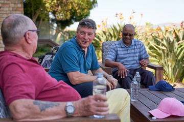 Mature male golfer friends talking and drinking water on patio