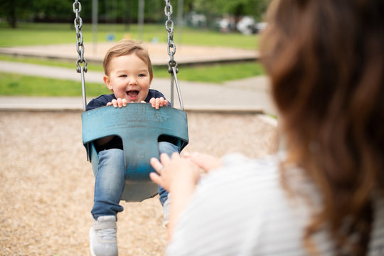 Mother pushing happy cute toddler girl in swing at playground
