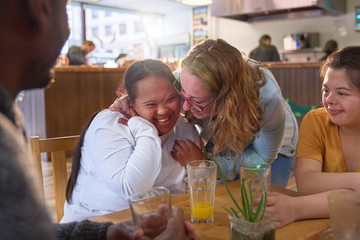 Happy mentor and young women with Down Syndrome laughing in cafe
