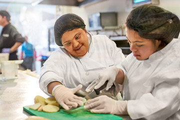 Smiling young women with Down Syndrome cutting potatoes in kitchen