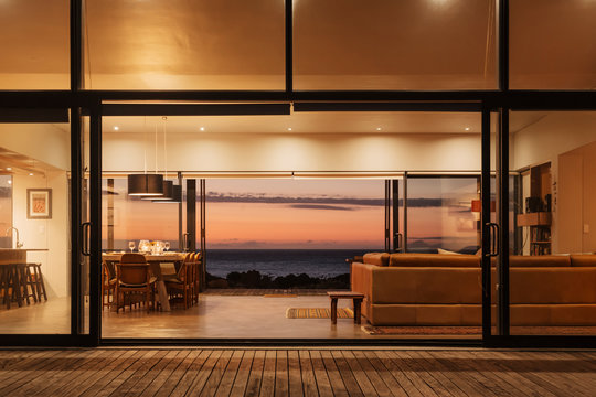 Illuminated home showcase interior overlooking ocean at sunset