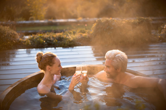 Couple toasting champagne glasses soaking in hot tub on autumn patio