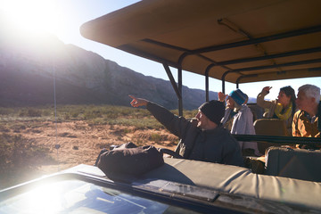 Safari tour guide and group in sunny off-road vehicle