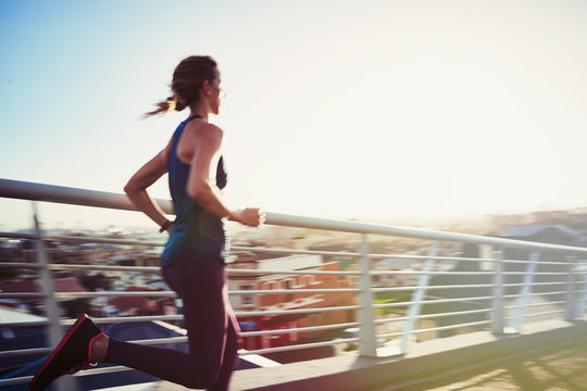 Female runner running on sunny urban footbridge
