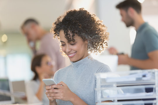 Smiling businesswoman texting with cell phone in office
