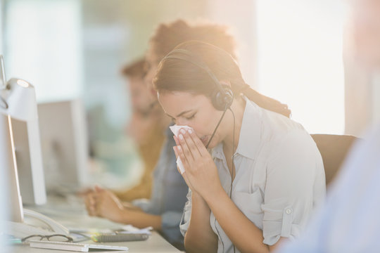 Businesswoman with headset blowing nose at computer in work