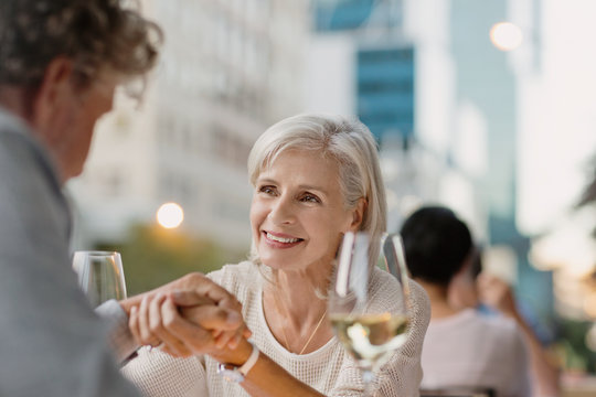 Affectionate senior couple holding hands drinking white wine at urban sidewalk cafe