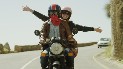 Exuberant young woman riding motorcycle on sunny road