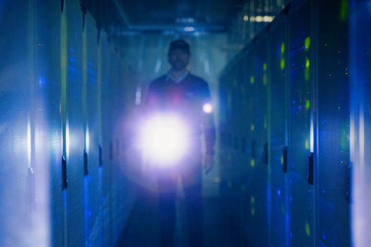 Server room technician with flashlight in dark corridor