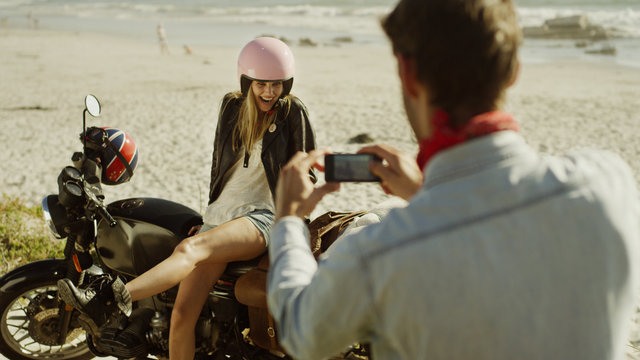 Young man photographing woman on motorcycle at beach
