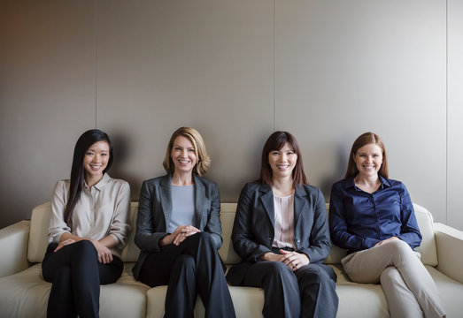 Portrait smiling businesswomen sitting in a row on sofa