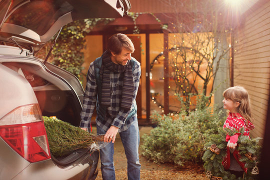 Father And Daughter Unloading Christmas Tree From Car Outside House