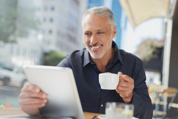 Smiling businessman using digital tablet drinking coffee at urban sidewalk cafe