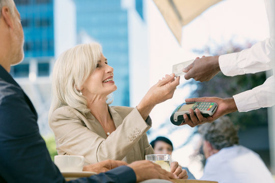 Businesswoman paying waiter with credit card reader at urban sidewalk cafe