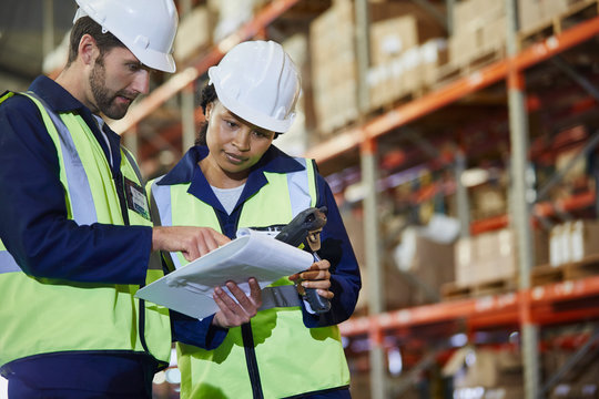 Workers with scanner and clipboard talking in distribution warehouse