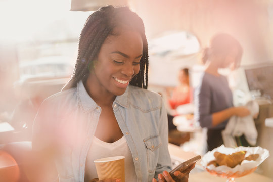 Smiling woman using cell phone and drinking coffee in cafe