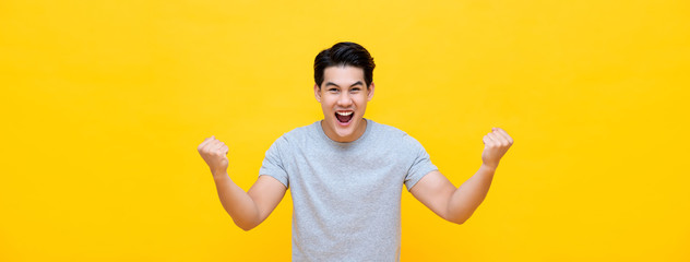 Excited young Asian man raising his fists with smiling delighted face