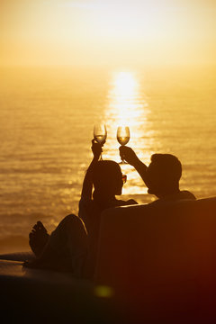 Silhouette couple toasting wine glasses on balcony with tranquil sunset ocean view
