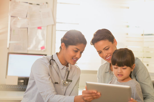 Female pediatrician showing digital tablet to girl patient and mother in examination room