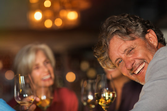 Portrait Laughing Senior Man Drinking White Wine With Friends At Bar