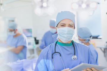 Portrait confident female surgeon wearing surgical mask using digital tablet in operating room