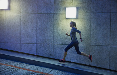 Female runner running ascending illuminated urban ramp