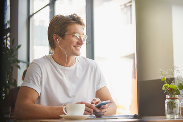 Smiling man with headphones and mp3 player listening to music drinking coffee in cafe