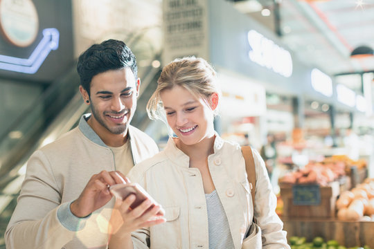 Smiling young couple using cell phone in grocery store market