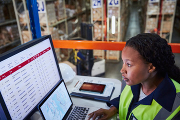 Focused female manager using laptop and computer in distribution warehouse