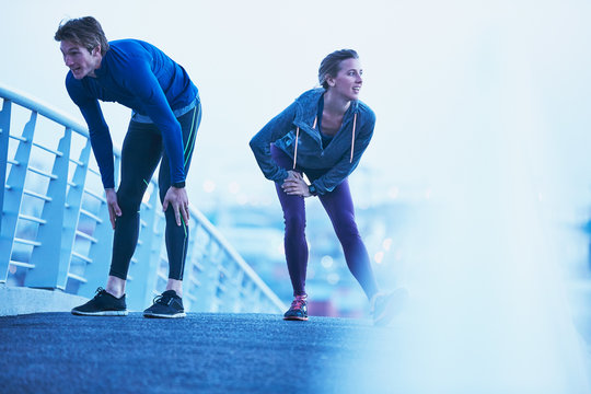 Runner couple stretching legs on footbridge