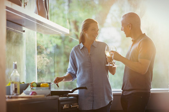Couple toasting white wine glasses, cooking in kitchen