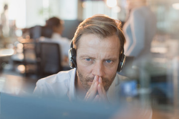 Serious businessman wearing headphones, working at computer