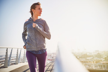 Female runner running on sunny urban footbridge at sunrise