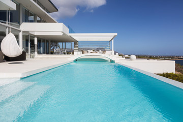 Sunny, tranquil modern luxury home showcase exterior swimming pool and patio