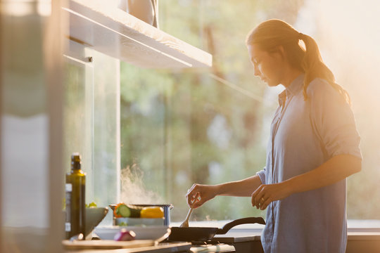 Woman cooking at stove in sunny kitchen
