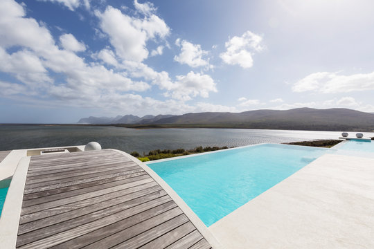 Sunny modern luxury infinity pool with footbridge and ocean view
